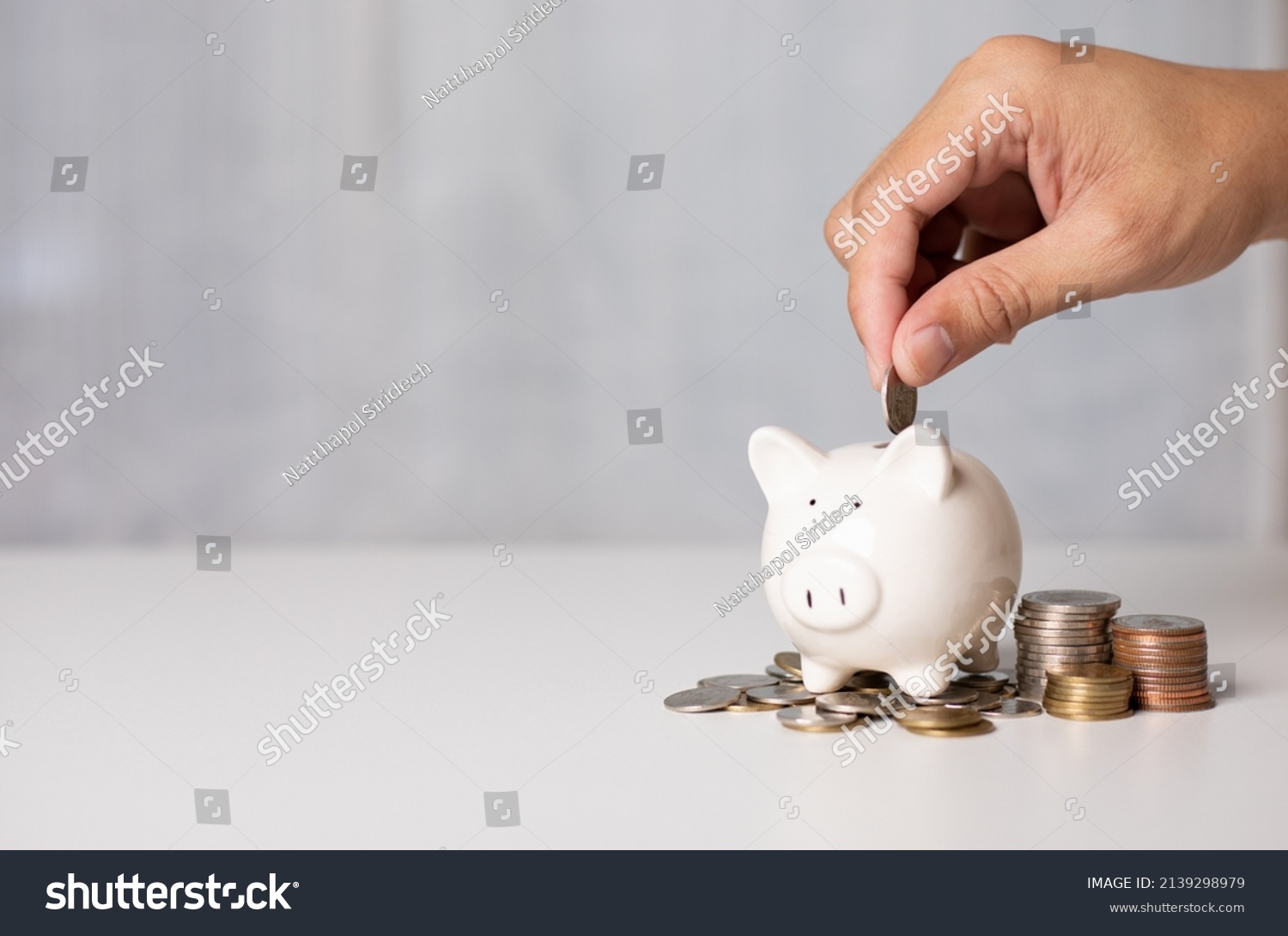 Hand putting a coin on pig saving. a pile of coins, business, investment, finance, and Money Saving for future concepts, save money. #2139298979
