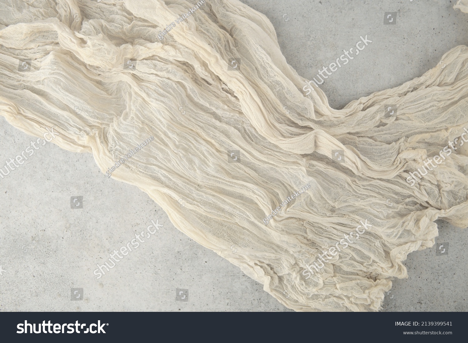Wrinkled gauze fabric on light grunge stone background. Cotton gauze fabric cloth on stone tile surface with copy space. #2139399541