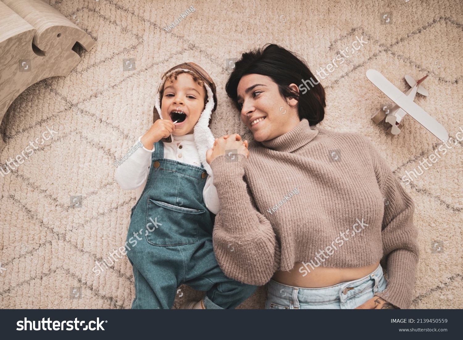 Happy family have fun at home. Mother and her son playing together. Boy dressed as a pilot while his mother holds his hand. Aerial view #2139450559