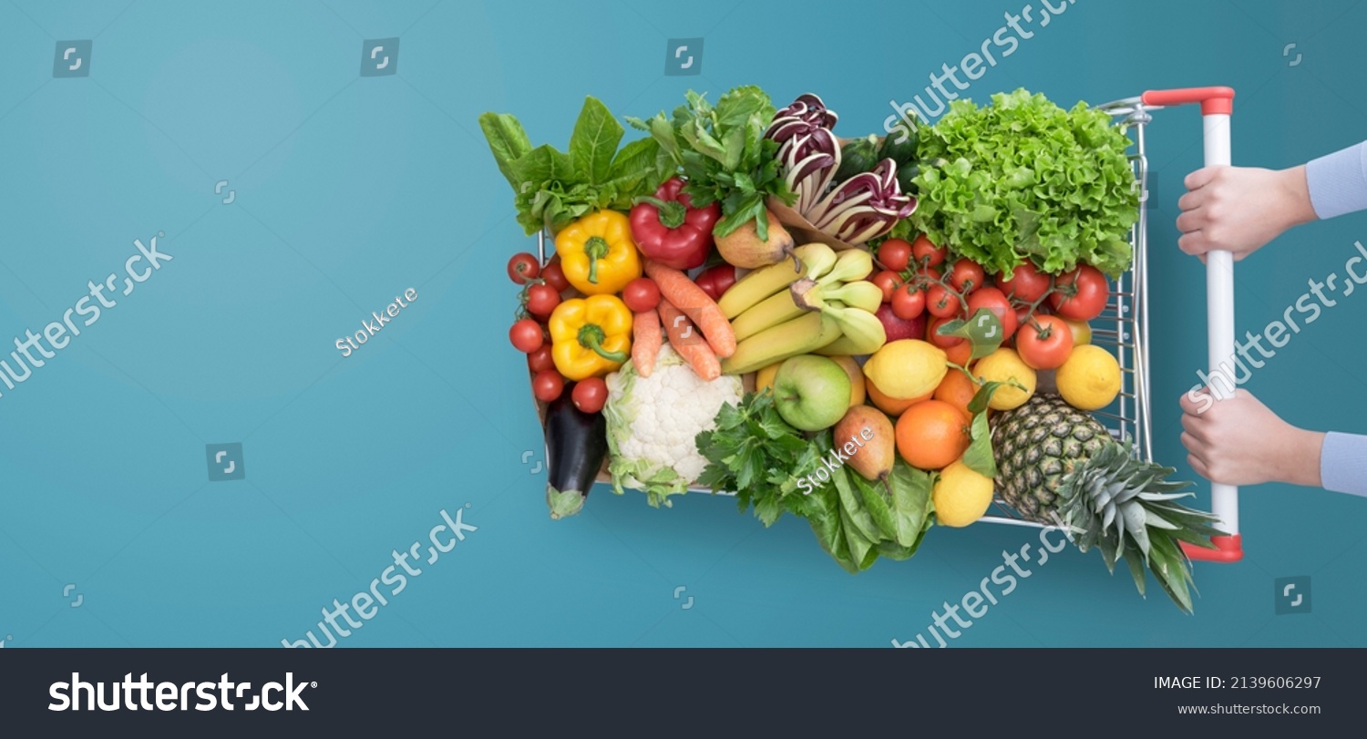 Woman pushing a shopping cart full of fresh delicious vegetables and fruits, grocery shopping concept, blank copy space #2139606297
