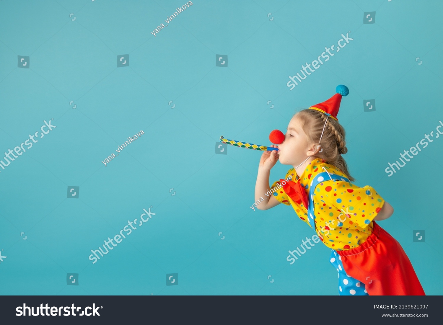 Funny kid clown against blue background. Happy child playing with festive decor. Birthday and 1 April Fool's day concept. #2139621097