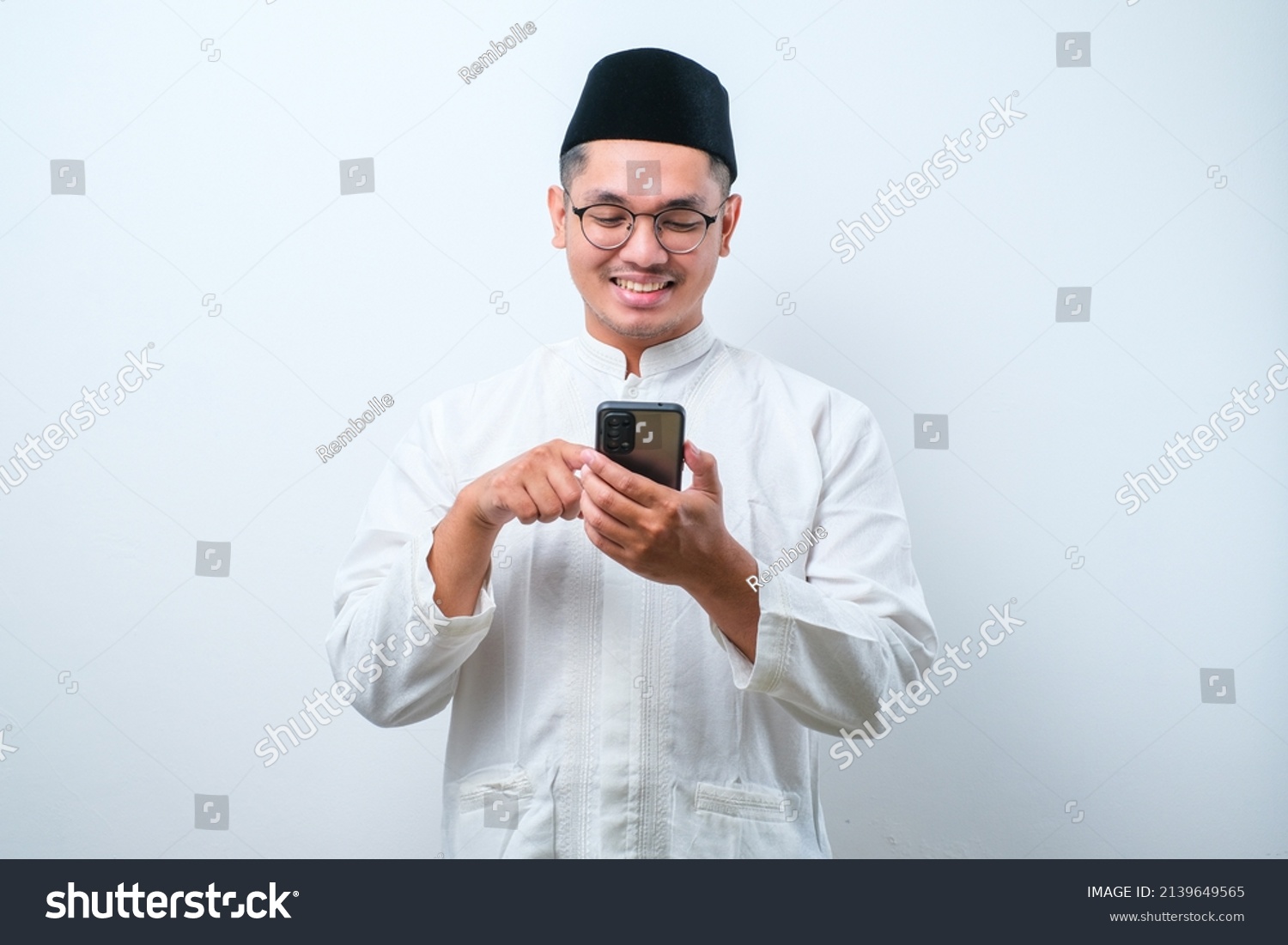 Happy asian muslim man holding and pointing on phone cellular over white background. Ramadan concept #2139649565