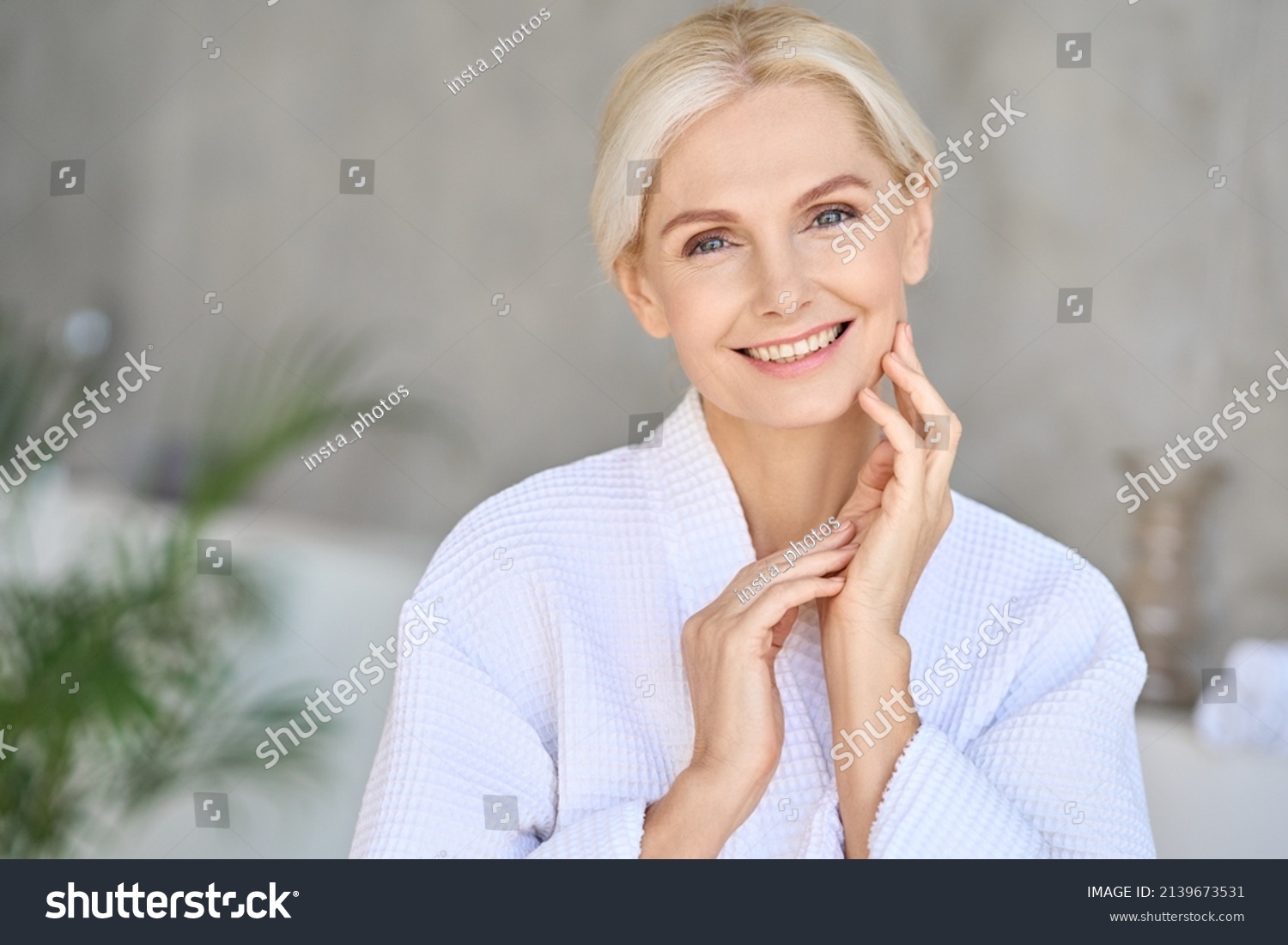 Headshot of happy smiling beautiful middle aged woman wearing bathrobe at spa salon hotel looking at camera touching face. Wellness spa procedures advertising. Skincare concept. #2139673531