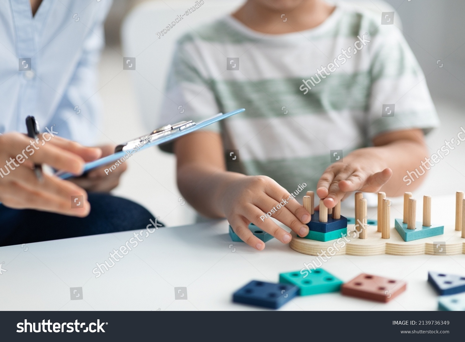 Kids development classes. Close up shot of unrecognizable little boy playing logical educational game during psychological consultation, specialist taking notes, empty space for text #2139736349