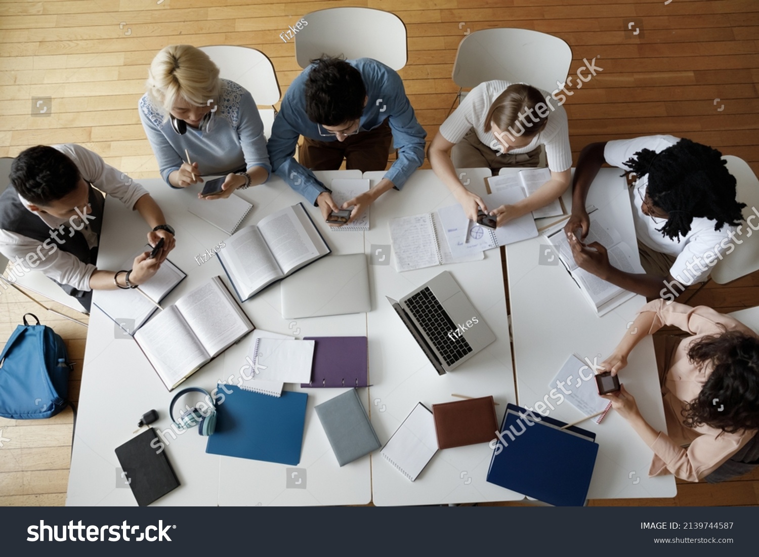 Overhead view group of multi ethnic students use smartphones sit at shared table in classroom. Mobile application usage at break, young gen Z modern wireless tech overuse, bad habit, lifestyle concept #2139744587