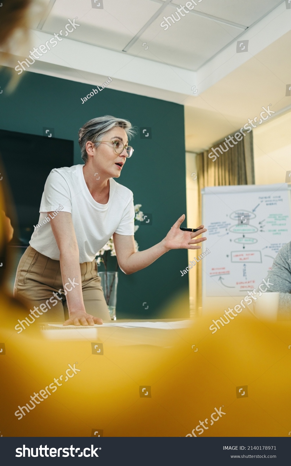 Experienced business professional leading a discussion with her team in a boardroom. Businesspeople sharing creative ideas during a meeting in a modern workplace. #2140178971