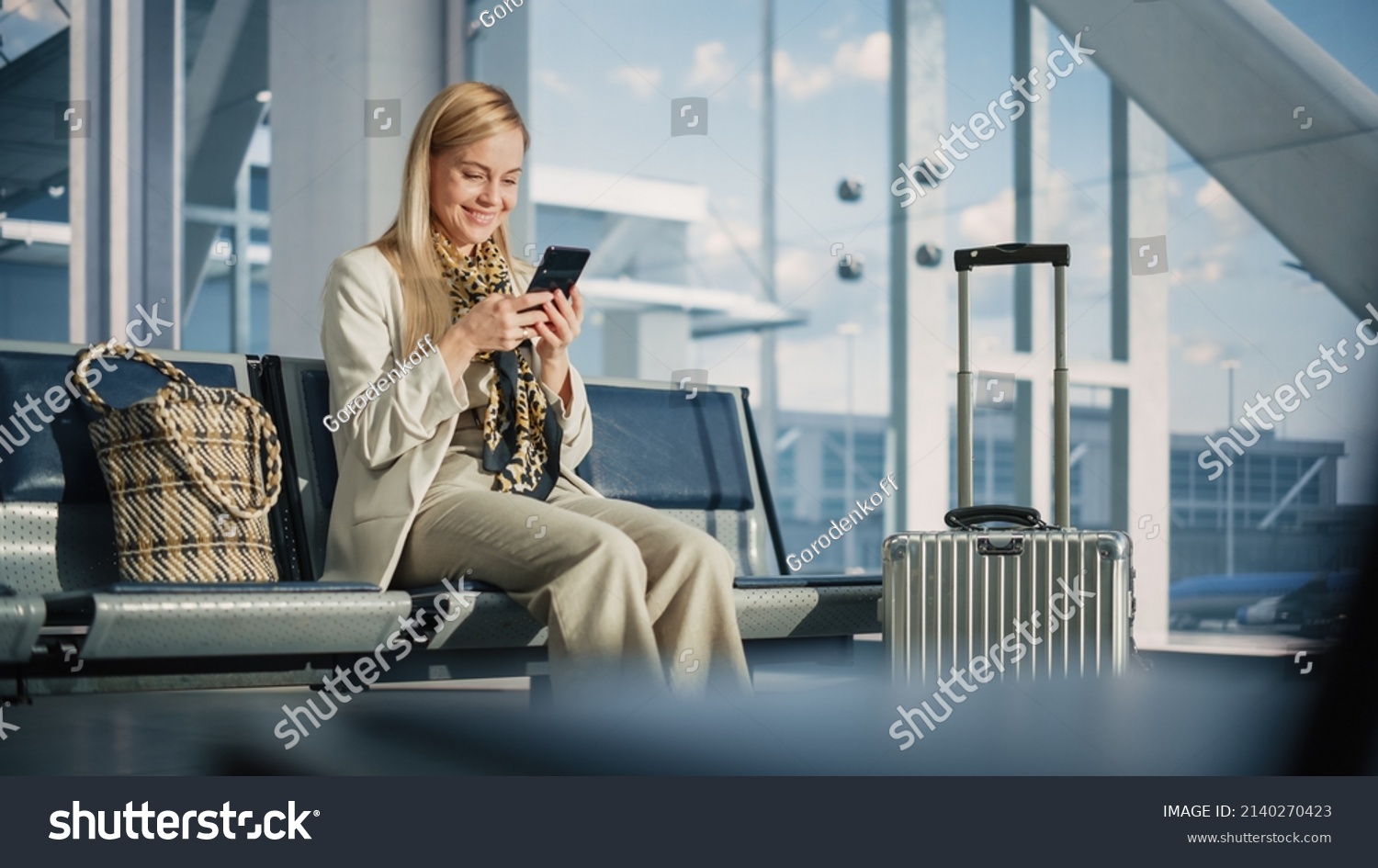 Airport Terminal: Woman Waits for Flight, Uses Smartphone, Browse Internet, Social Media, Online Shopping. Traveling Female Remote Work Online on Mobile Phone in a Boarding Lounge of Airline Hub #2140270423