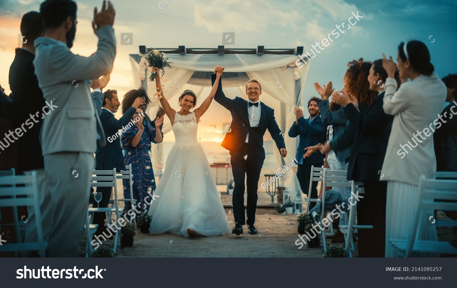 Beautiful Bride and Groom Celebrate Wedding Outdoors on a Beach Near the Ocean at Sunset. Perfect Marriage Venue with Best Multiethnic Diverse Friends Throwing Flower Petals on the Newlyweds. #2141095257