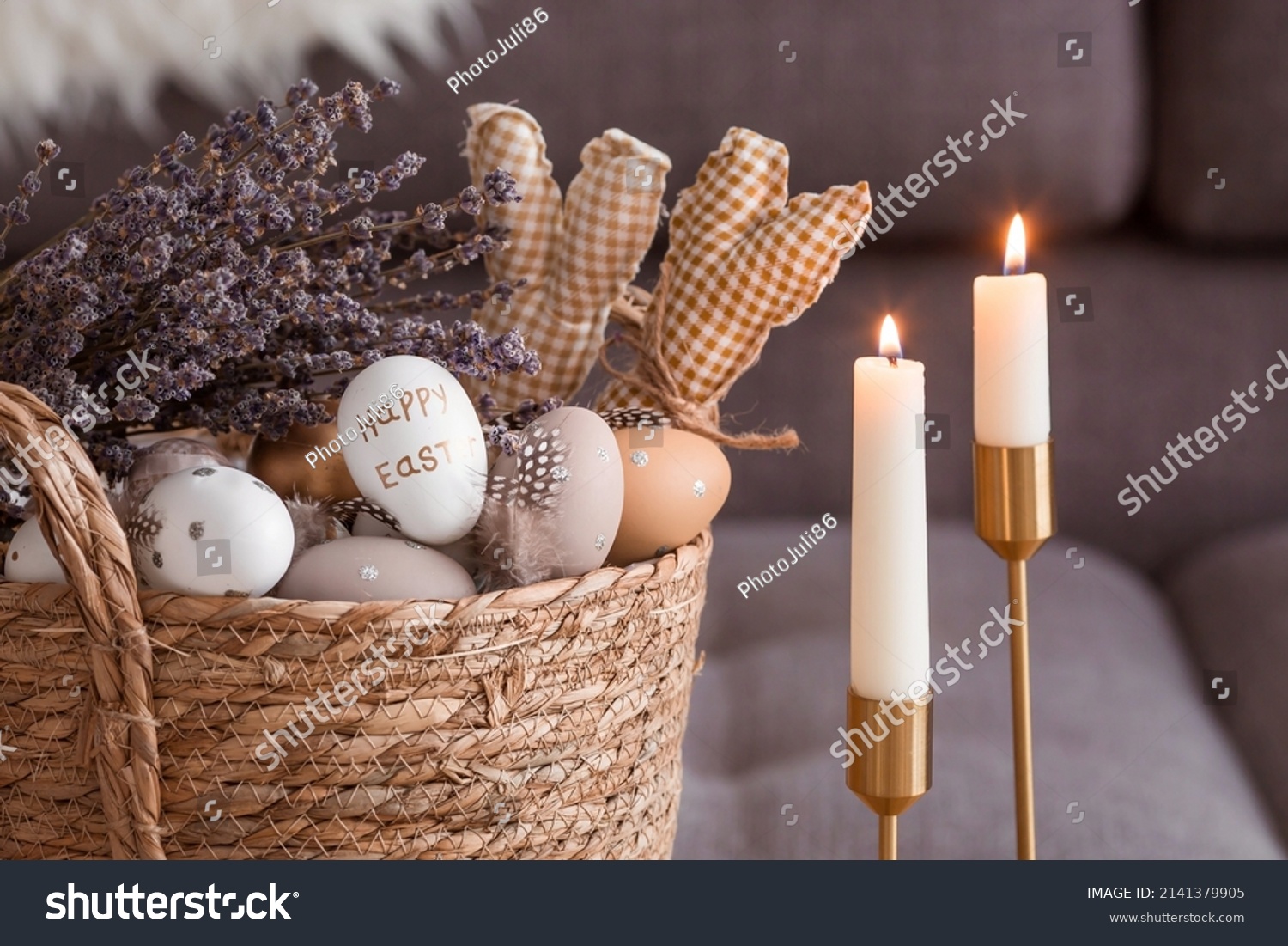 Provence. A wicker basket with Easter eggs, lavender and burning candles in the interior of the living room on a wooden table. The concept of home comfort in the bright holiday of Easter 2022. #2141379905