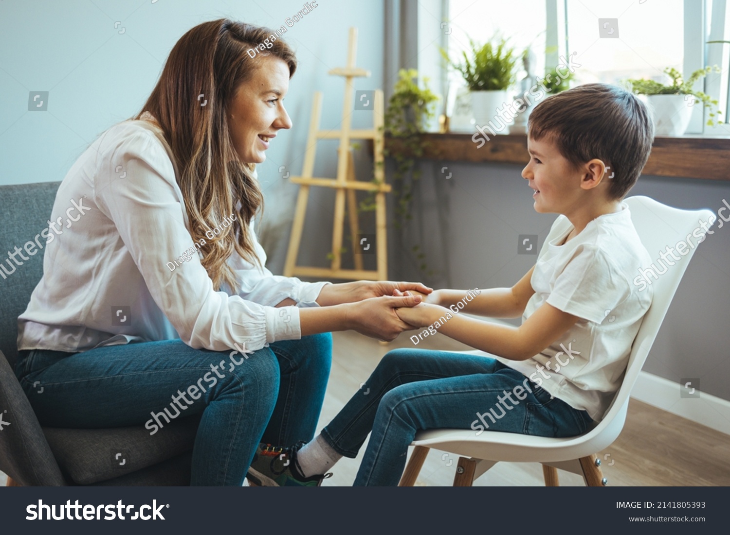 Shot of a little boy talking to a psychologist. Attentive and sympathetic woman psychologist listens to little boy. Notes to himself in clipboard. Mental health. #2141805393