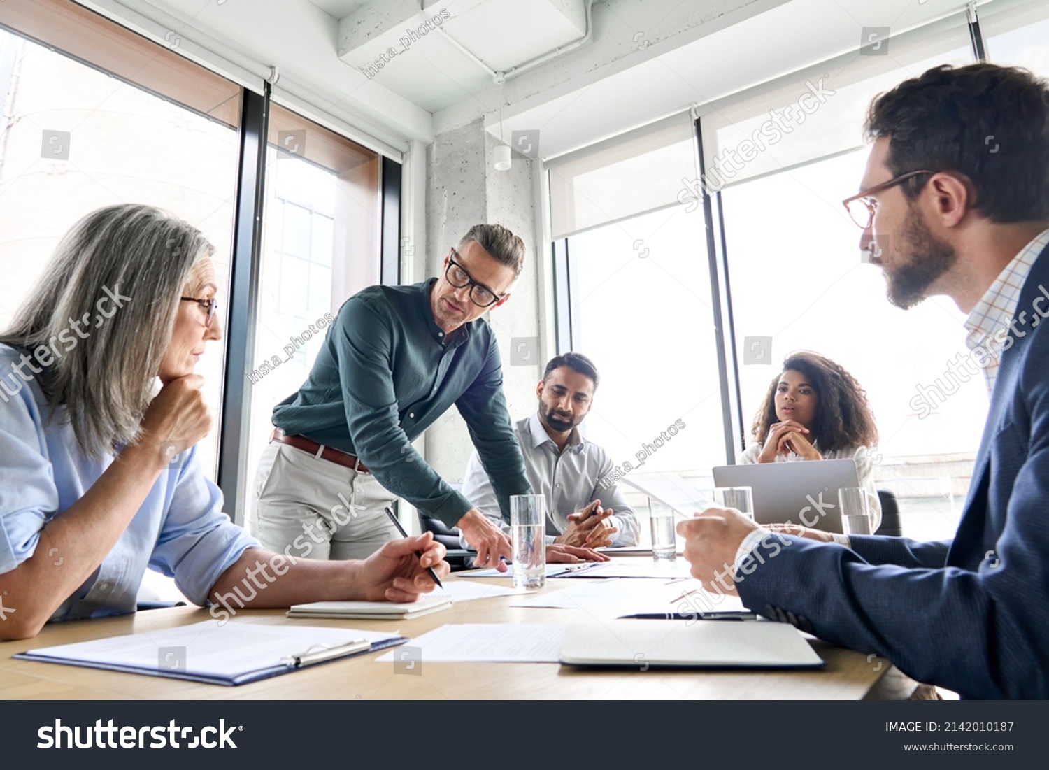 Male mature caucasian ceo businessman leader with diverse coworkers team, executive managers group at meeting. Multicultural professional businesspeople working together on research plan in boardroom. #2142010187