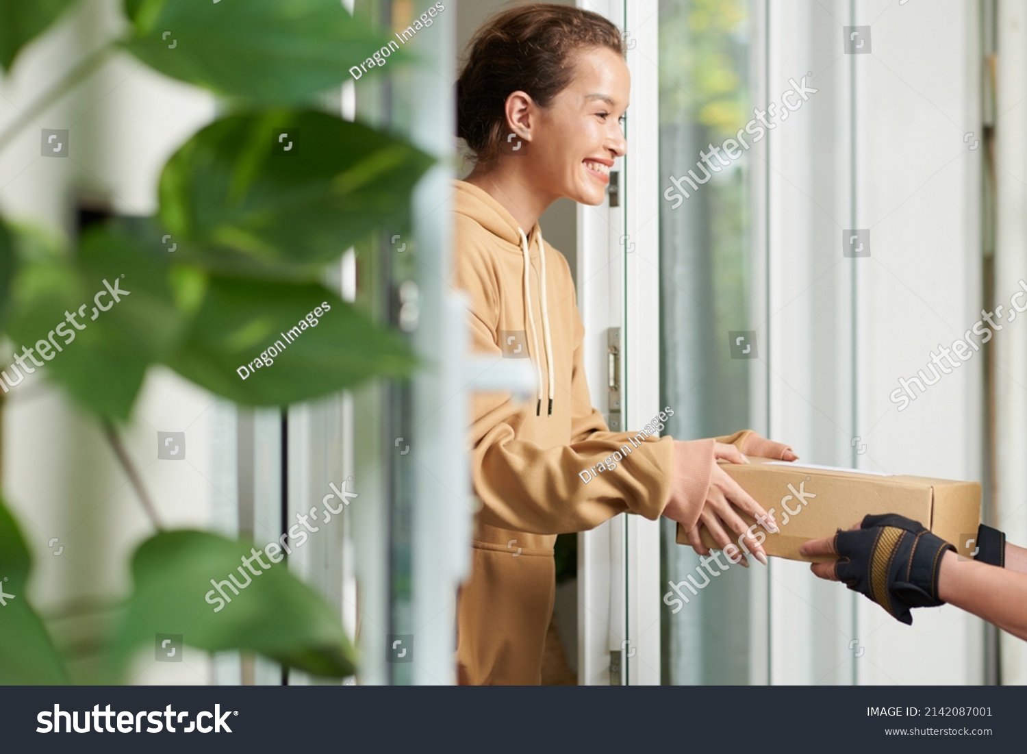 Happy excited young woman receiving package that delivery man brought to her house #2142087001