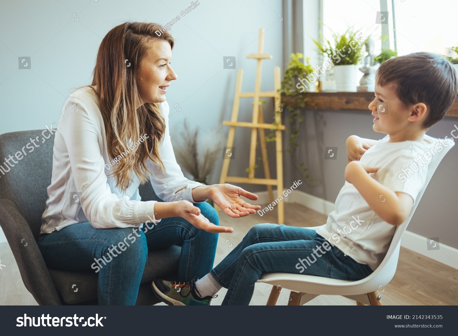 Cheerful young kid talking with helpful child counselor during psychotherapy session in children mental health center. Child counselor during psychotherapy session #2142343535