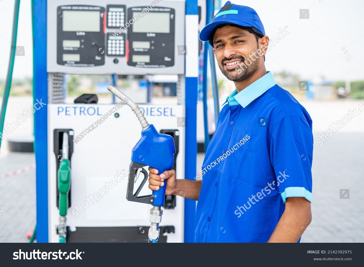 Happy petrol pump worker standing by holding fuel nozzle while looking camera at gas filling station - concept of happiness, job and petroleum service. #2142392975