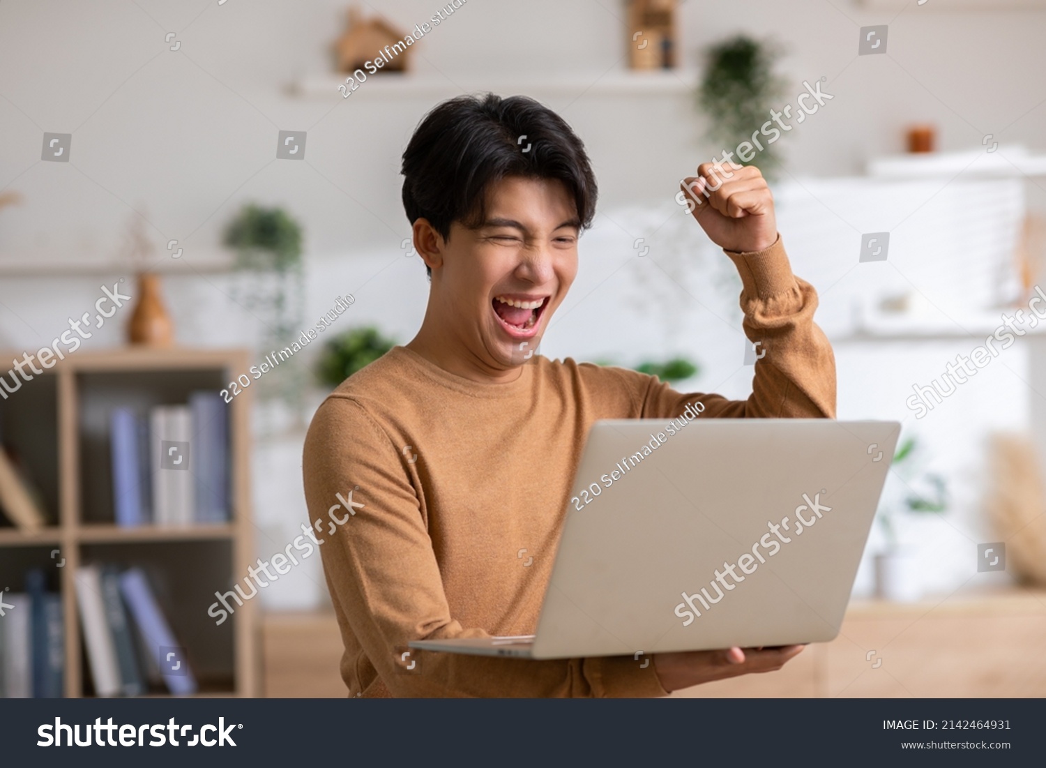 Asian man is smiling and expressing happy feeling on the computer laptop screen. young male got good news and show his cheerful face.Happiness men looking on laptop read message feel excited at home #2142464931