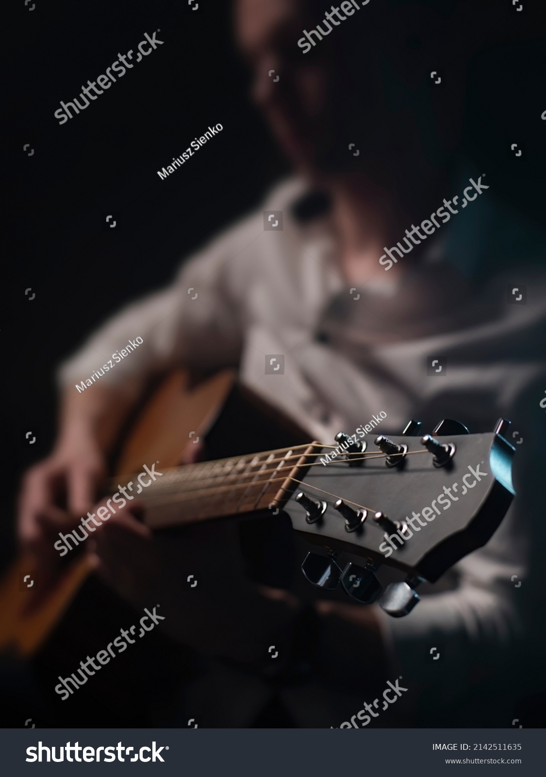 The guitarist is playing acoustic guitar shown in small depth of field where the focus is on the headstock. Dark and moody. #2142511635