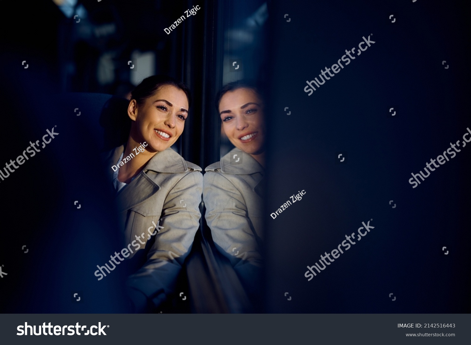 Happy woman looking through window while enjoying her train journey. The view is through passengers seats. Copy space.  #2142516443