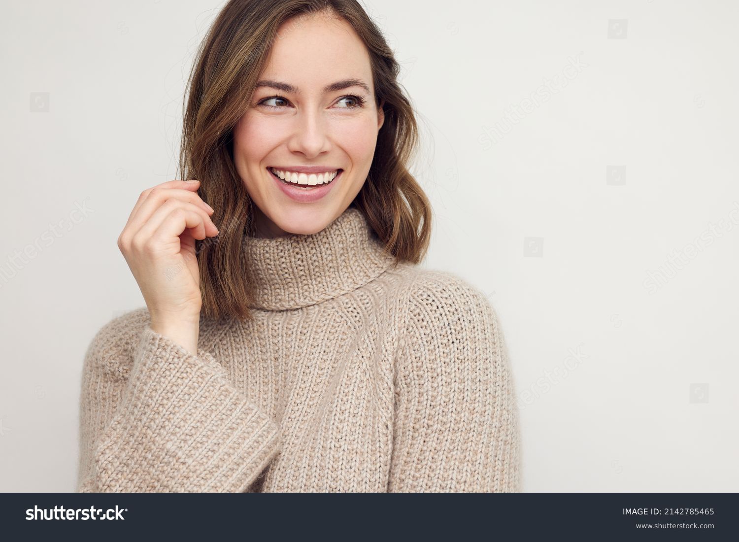 Portrait of young happy beautiful woman smiling and standing isolated on white background in a warm sweater. Young female girl with a perfect smile looking right. #2142785465