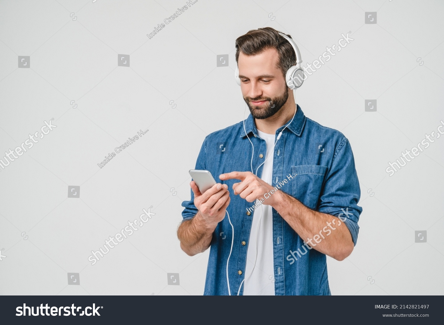 Caucasian young student man freelancer listening to the music in headphones, choosing sound track, song, playlist, podcast on phone isolated in white background #2142821497