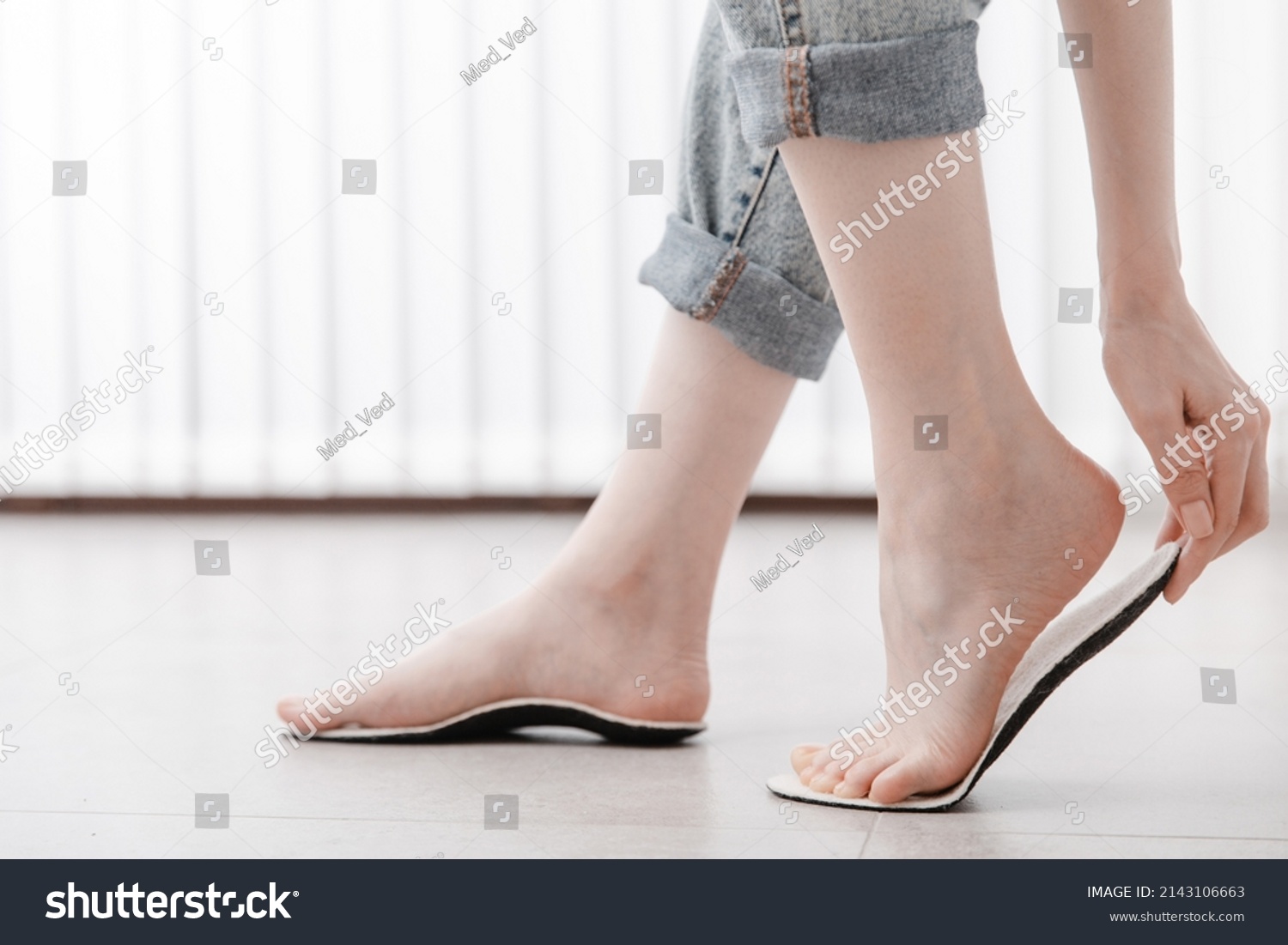 Woman fitting orthopedic insole indoors, close up. Girl holding an insole next to foot at home. Orthopedic insoles. Foot care banner. Flat Feet Correction. Treatment and prevention of foot diseases. #2143106663
