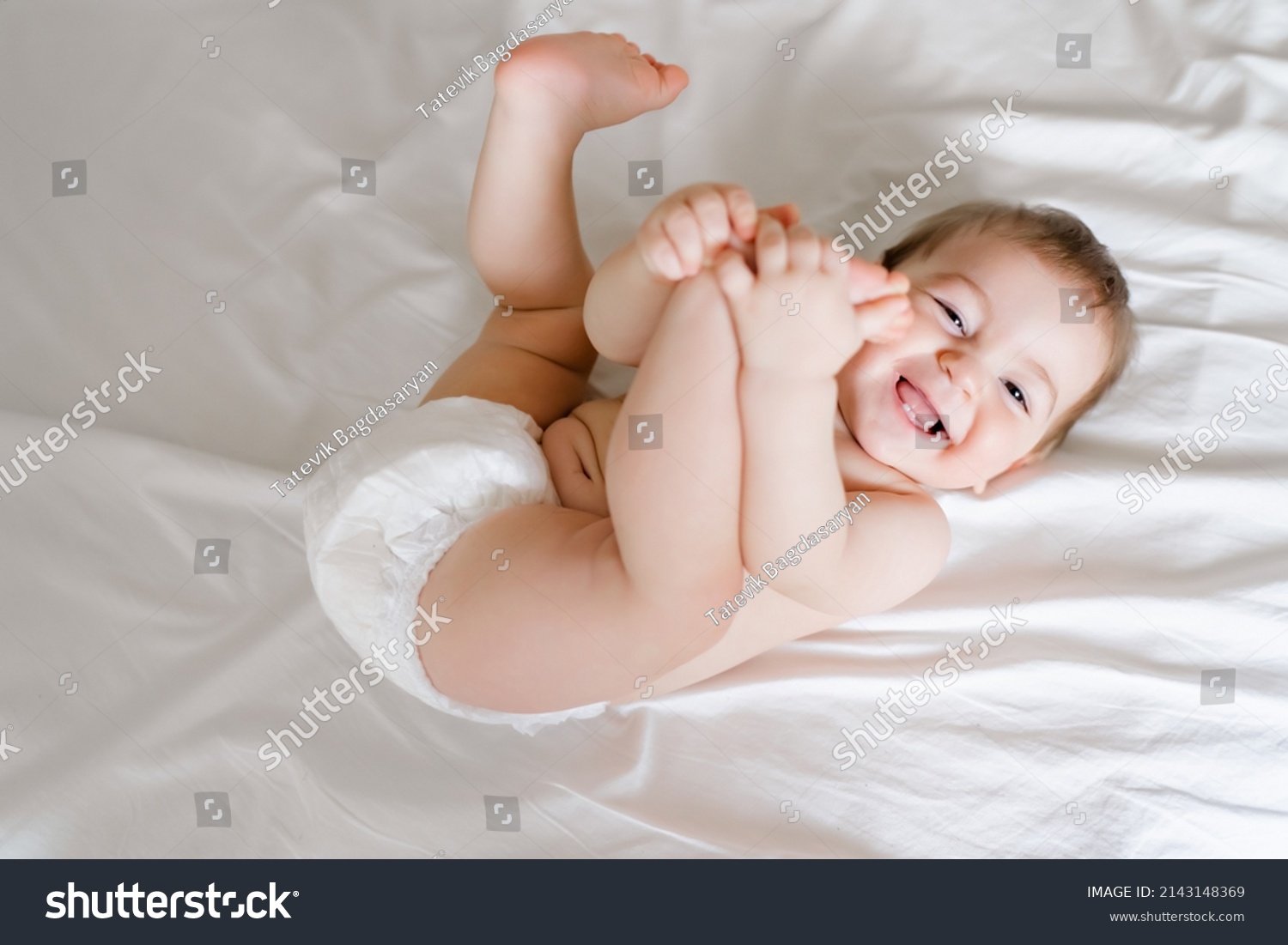 happy joyful baby in diapers lying on white bed #2143148369