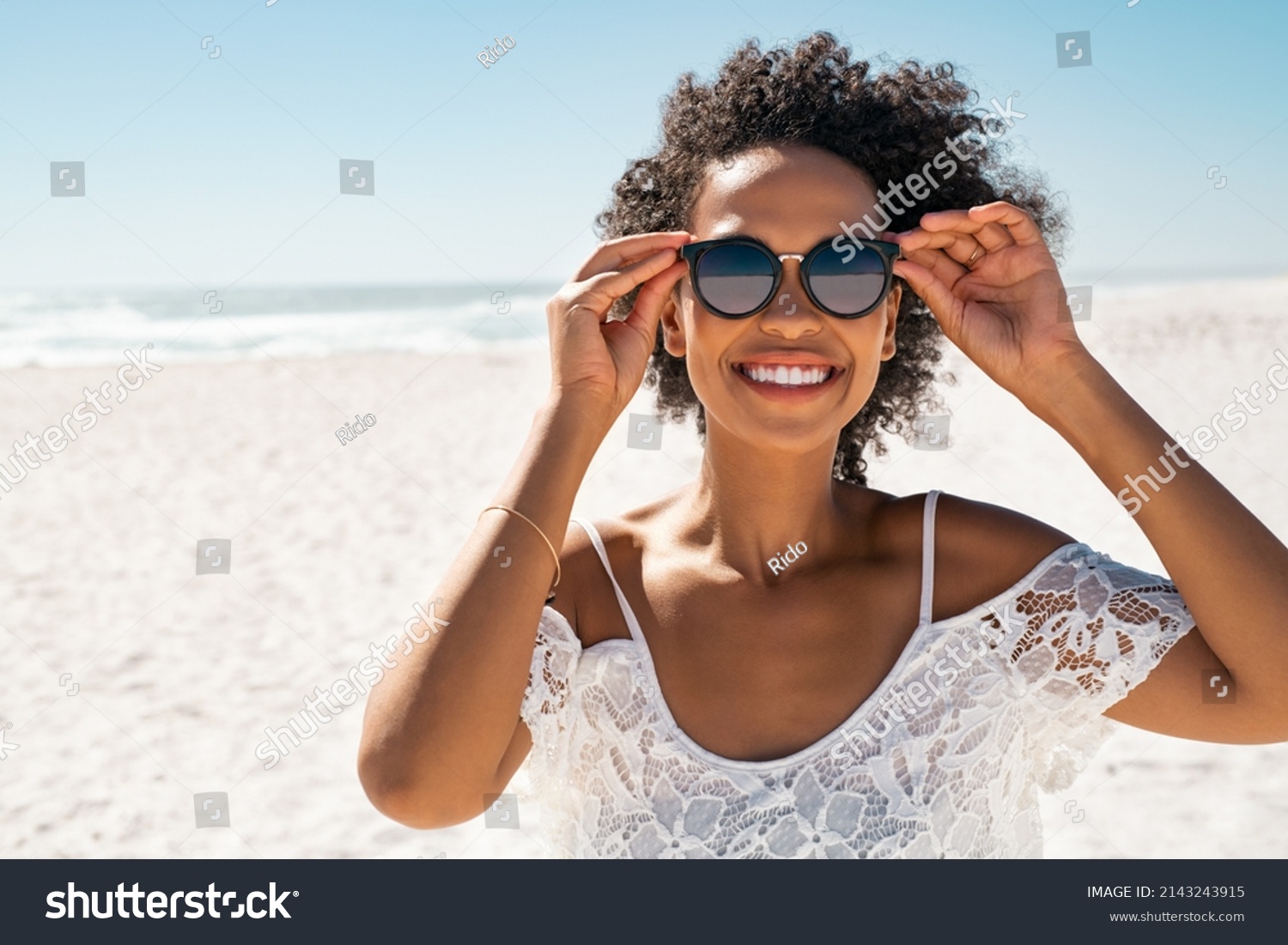 Portrait of smiling african american woman wearing sunglasses at the beach with copy space. Happy black girl wearing fashionable specs while smiling at seaside. Beautiful woman relaxing at sea. #2143243915