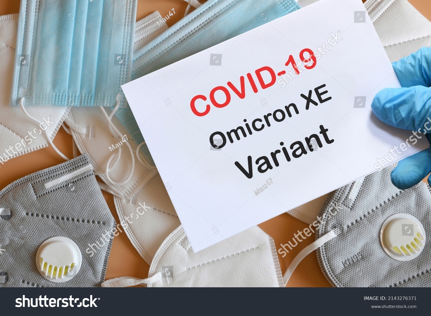 Doctor's hand in blue glove with white paper and text Covid-19 Omicron XE Variant with various protection masks on background. COVID-19 Omicron XE Variant strain protection concept. #2143276371