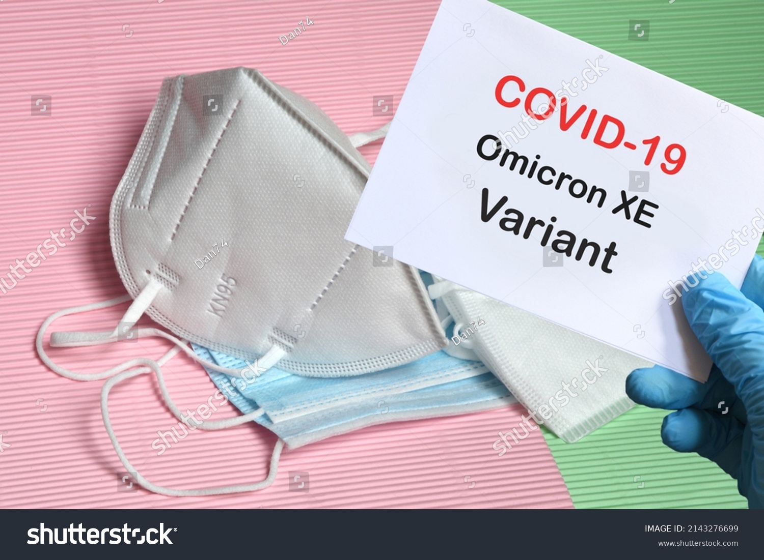 Doctor's hand in blue glove with white paper and text Covid-19 Omicron XE Variant with various protection masks on background. COVID-19 Omicron XE Variant strain protection concept. #2143276699