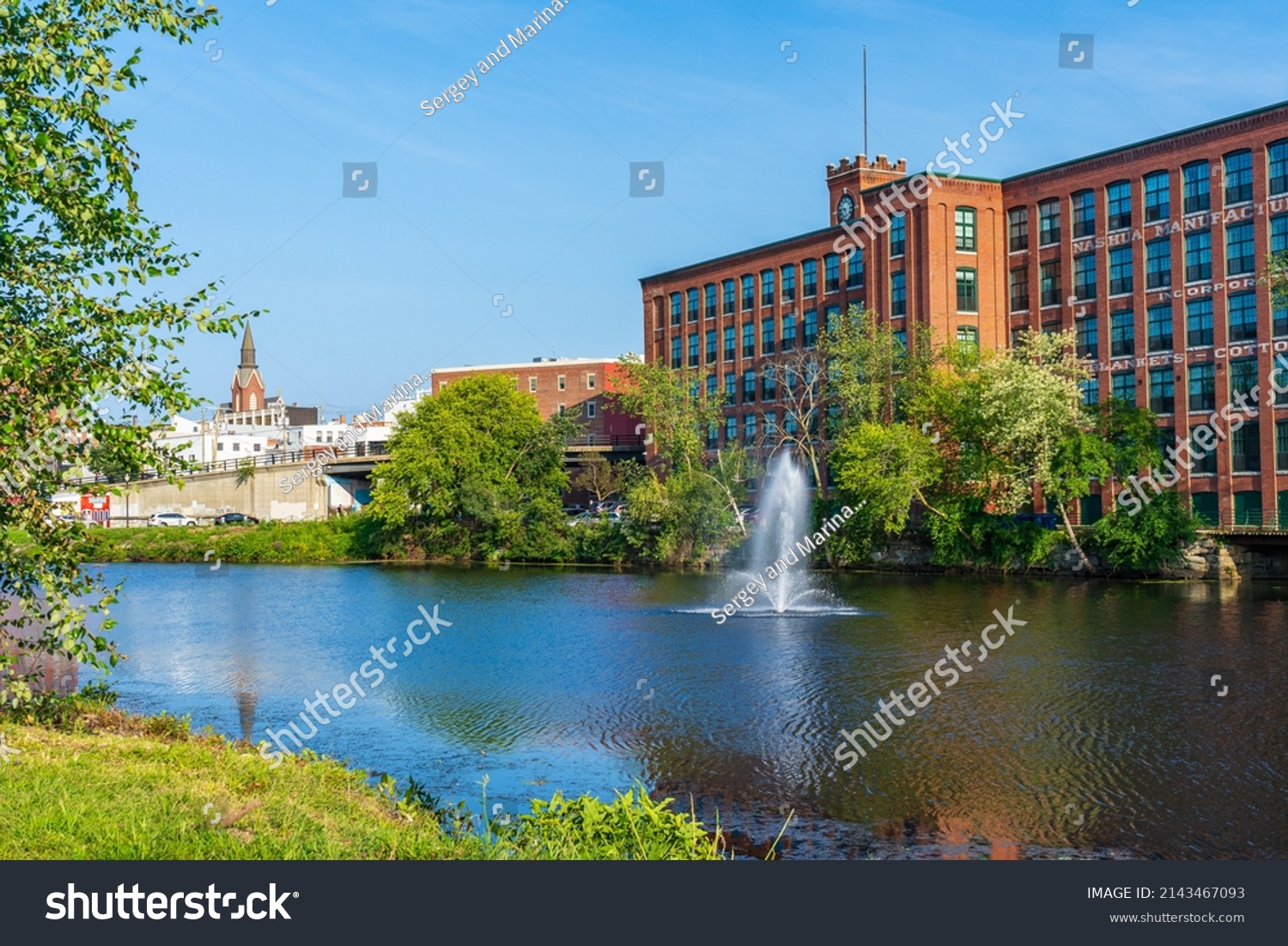 Fountain on the Nashua River against the background of a historic cotton factory building with a clock tower in the old industrial park of Nashua. New Hampshire, USA #2143467093