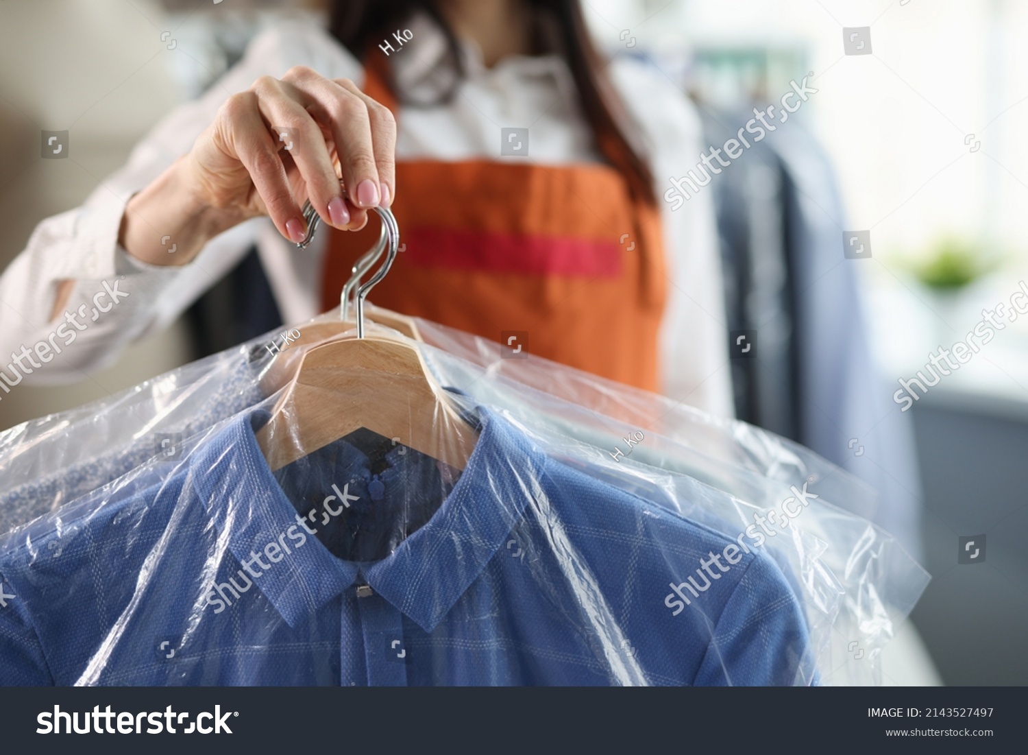 Administrator at dry cleaners keeps clean clothes on hangers in bag #2143527497