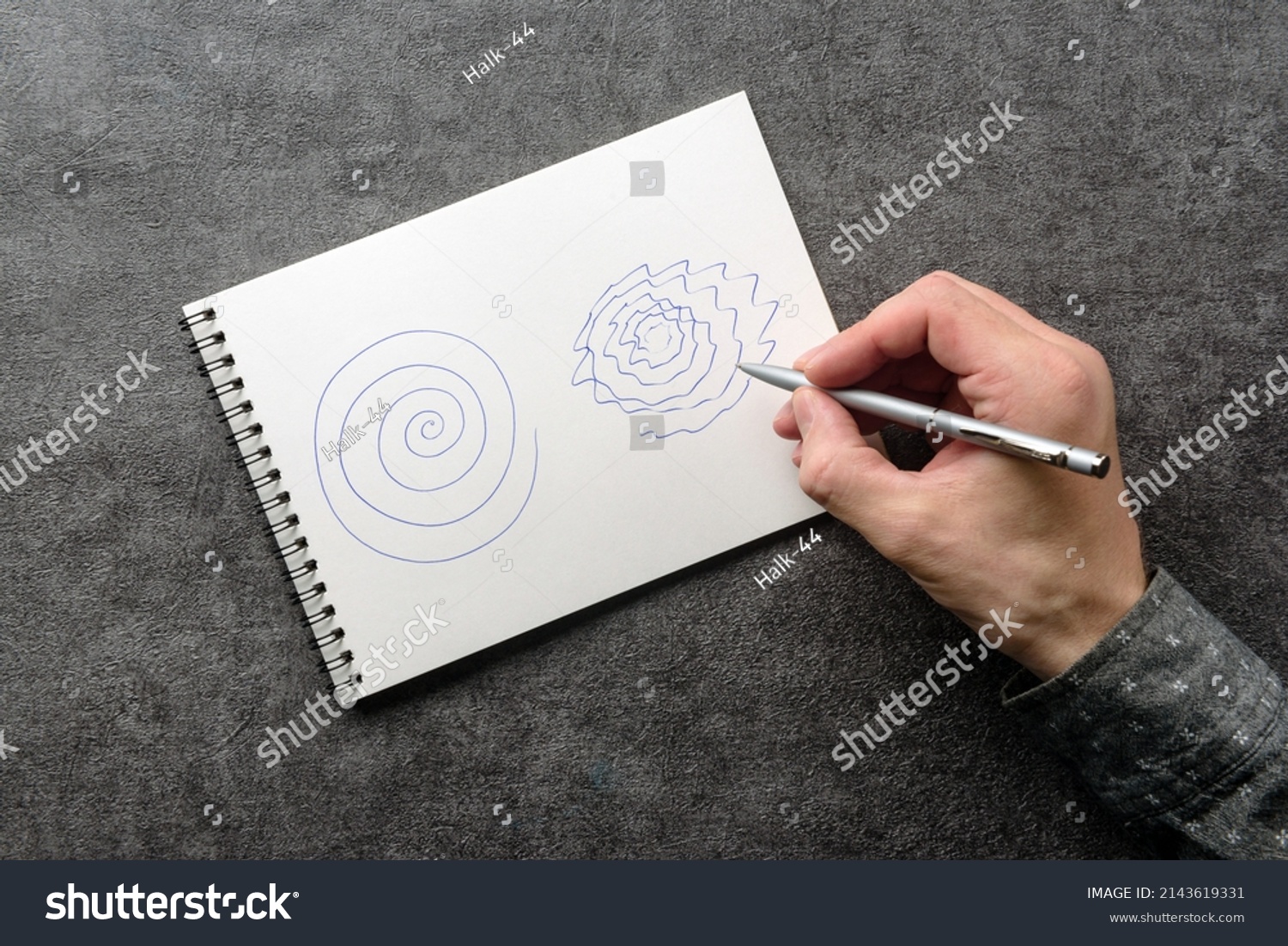 A man with trembling hands is trying to repeat the spiral drawing in a notebook. Test for essential tremor and parkinson's disease. #2143619331
