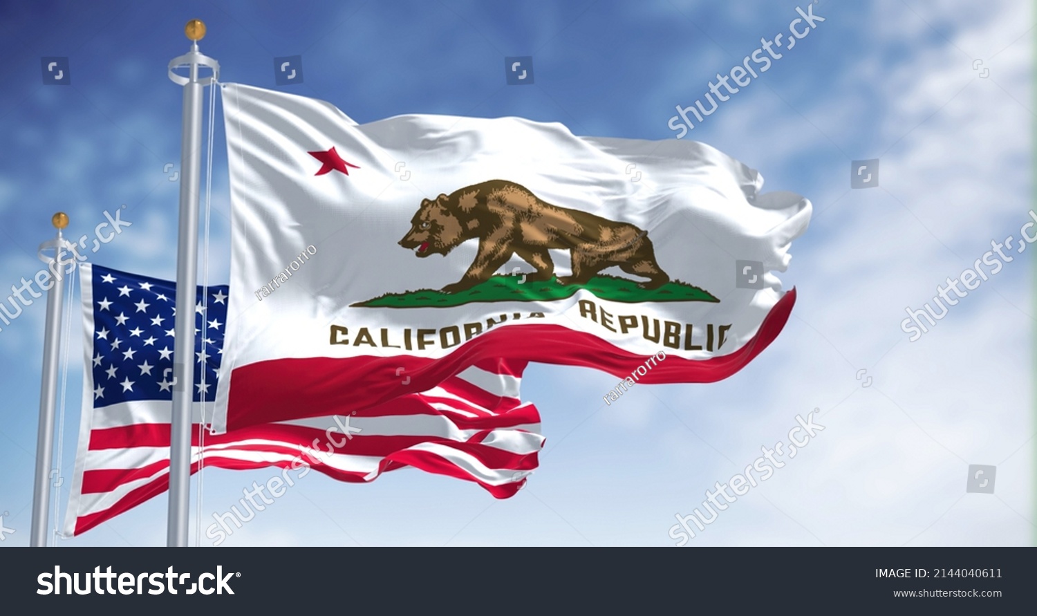 The California state flag flying along with the national flag of the United States of America. In the background there is a clear sky. The flag depicts a walking bear and a five-pointed red star #2144040611