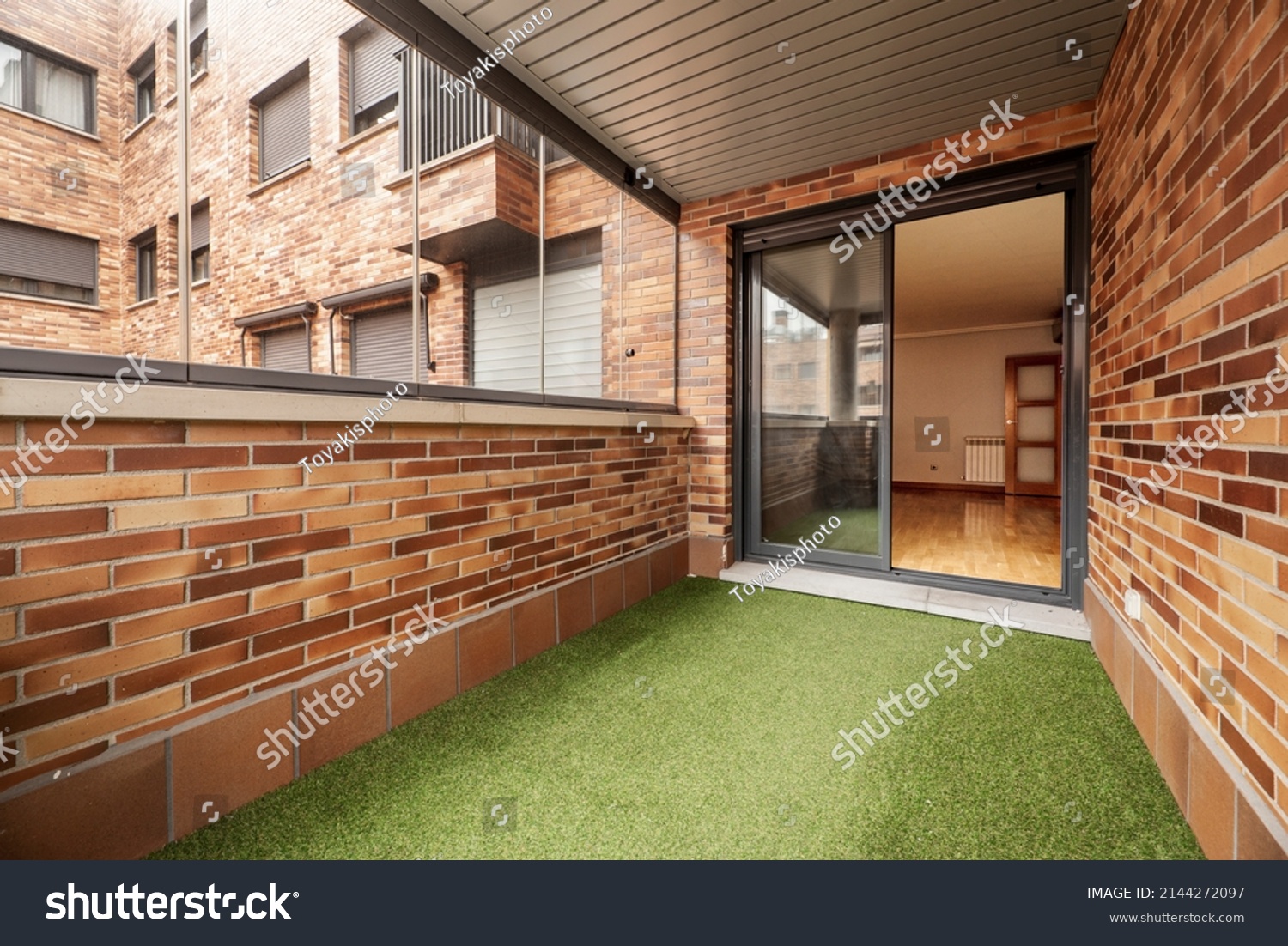 Enclosed terrace with glass and metal, brown bricks and green artificial grass floor in urban residential housing #2144272097