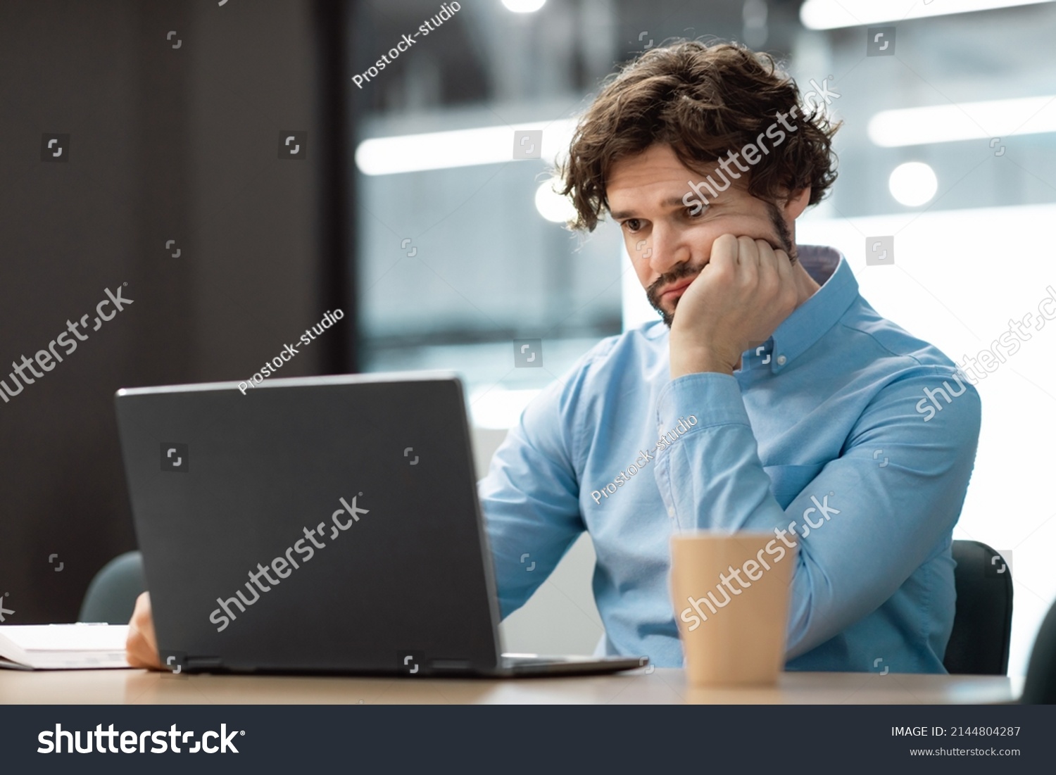 Portrait of sad bored business man sitting at desk using pc, leaning head on hand looking at screen. Upset stressed guy suffering job problems, reading bad negative news at office, free copy space #2144804287