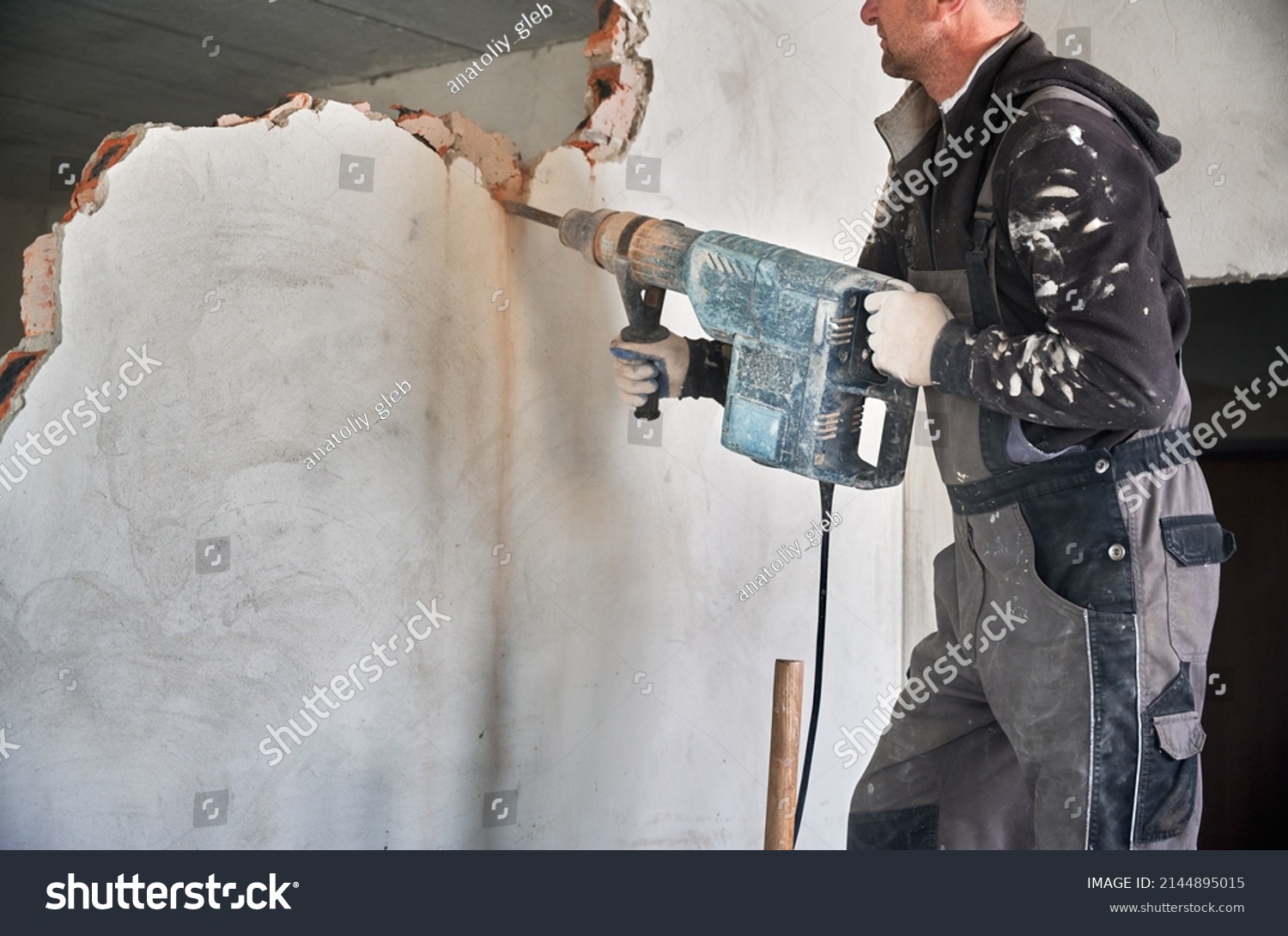 Close up of special powerful hand instrument with percussion mechanism for drilling and breaking walls. Man holding jackhammer and dismantling inner wall in room. #2144895015