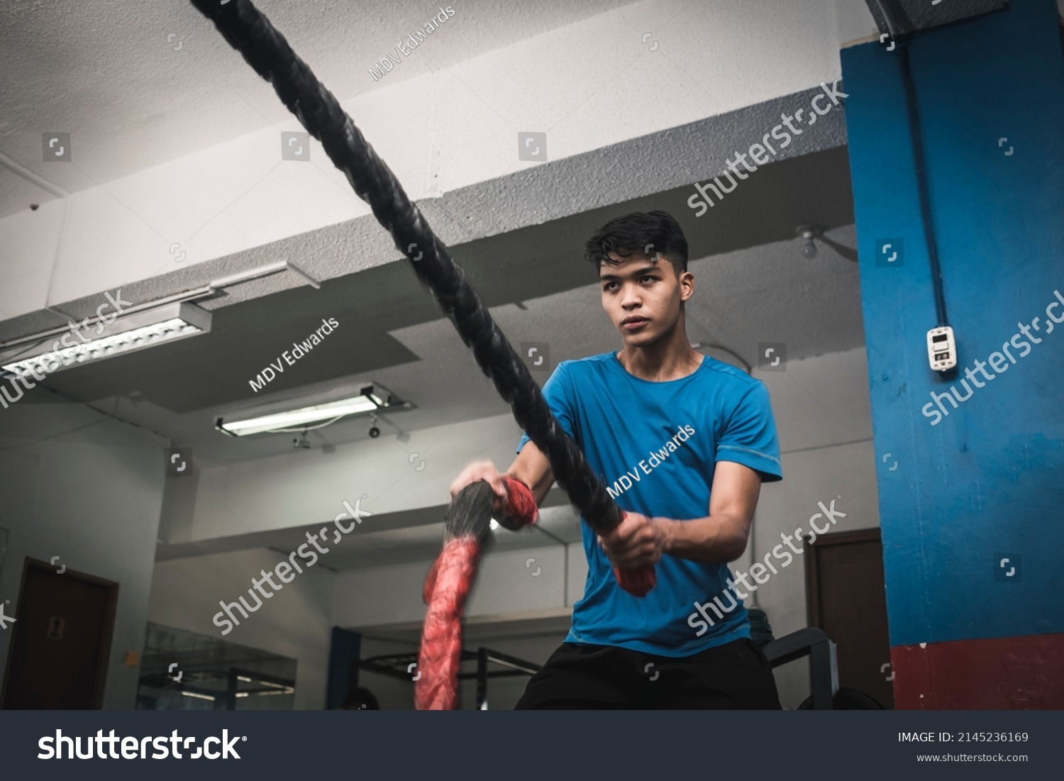 A fit young asian man doing an intense battle rope session. Cardiovascular training at the gym. #2145236169
