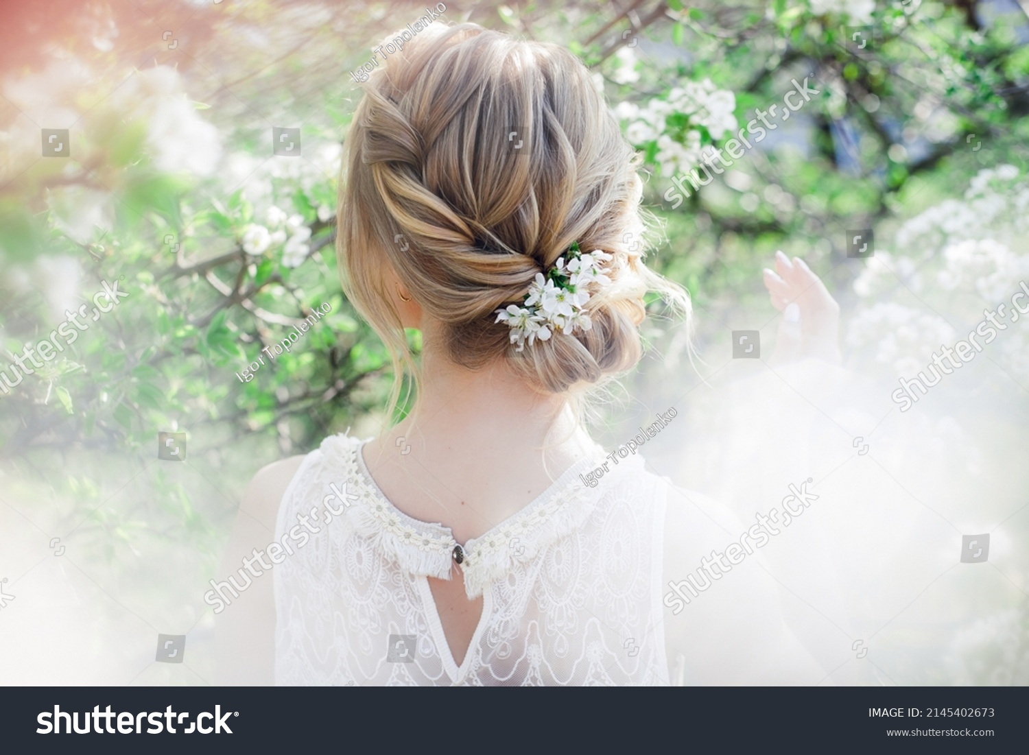 Art work hairstyles with weaving for a blonde bride in a blooming spring garden with green leaves #2145402673