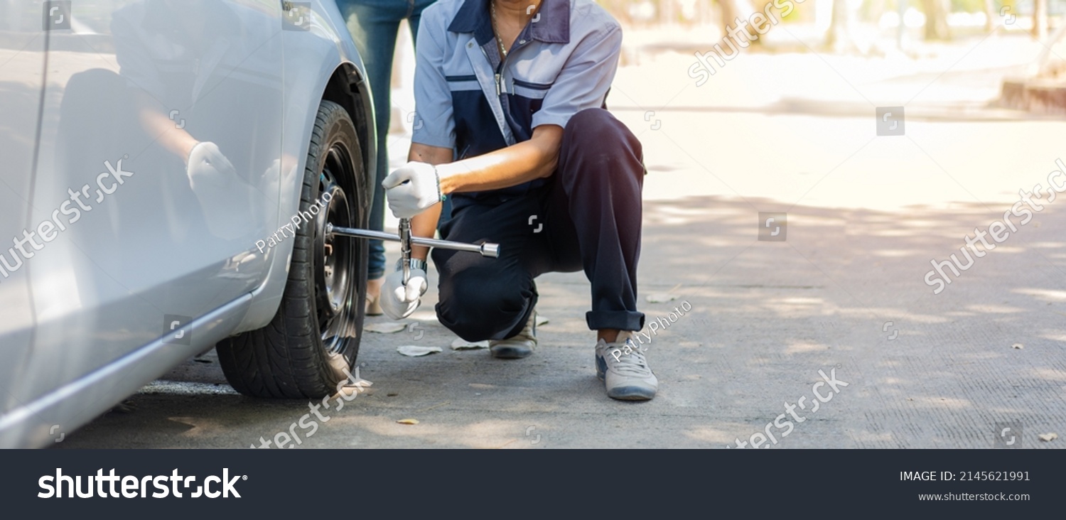 Expertise mechanic man  in uniform using force trying to unscrew the wheel bolts nuts and help a woman for changing car wheel on the highway, car service, repair, maintenance concept. #2145621991
