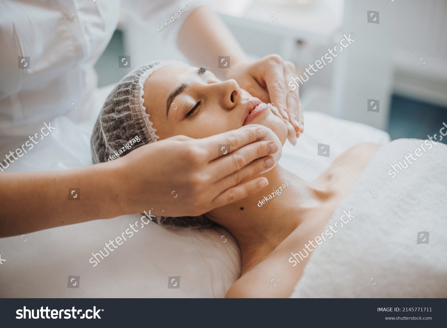 Facial skin treatment. Girl facial treatment. Facial skincare. Spa body care.Close up portrait of beautician's hands cleaning female face with cotton pads at #2145771711