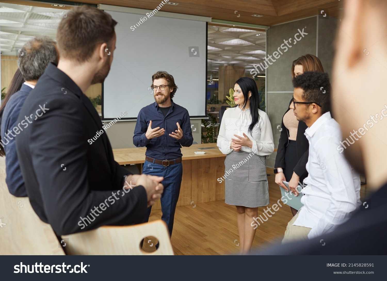 Business coach talking to group of people standing in office around him. Team of entrepreneurs and listening to business trainer speaking about creativity and teamwork, sharing advice and experience #2145828591