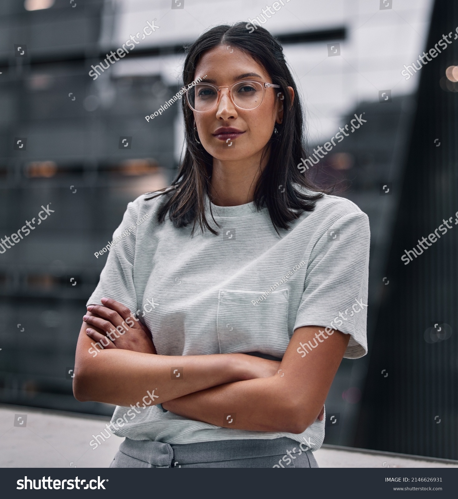 Determined to make it no matter the cost. Shot of an attractive young businesswoman standing alone in the office with her arms folded during a late shift. #2146626931