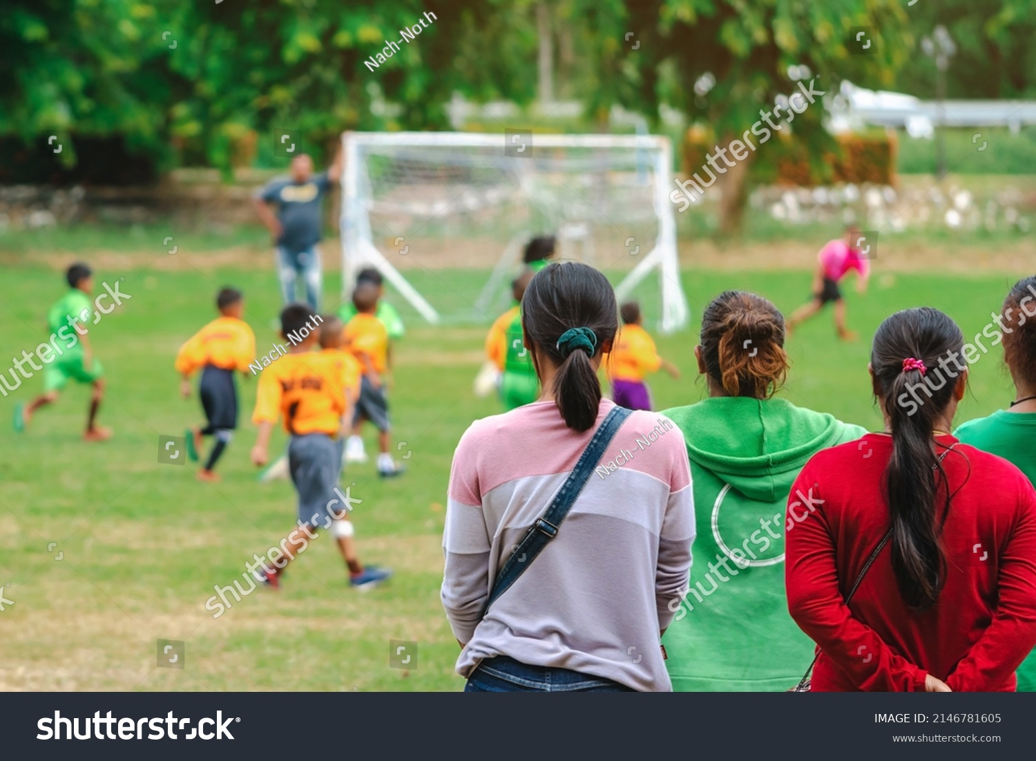 Back view of Moms watch and cheering their sons playing football in school tournament on sideline. Sport, outdoor active,  Spectator watching soccer game. Parents care and encourage their children. #2146781605