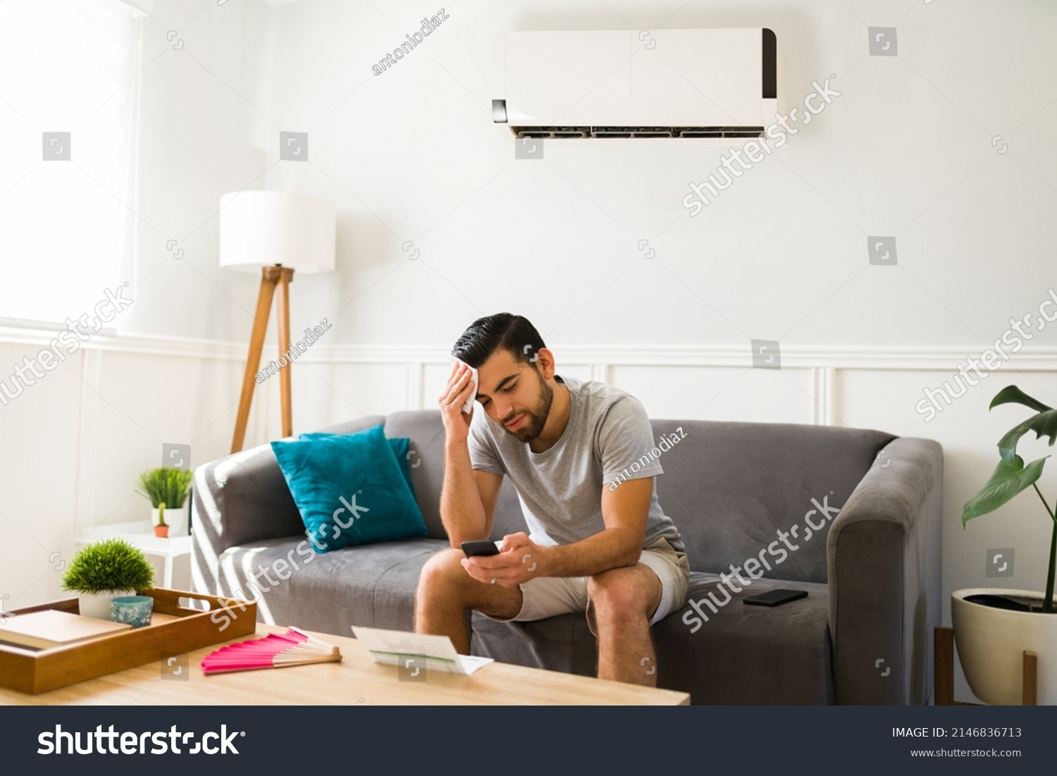 Upset man sweating during a heat wave in the summer while at home with a cold ac unit #2146836713