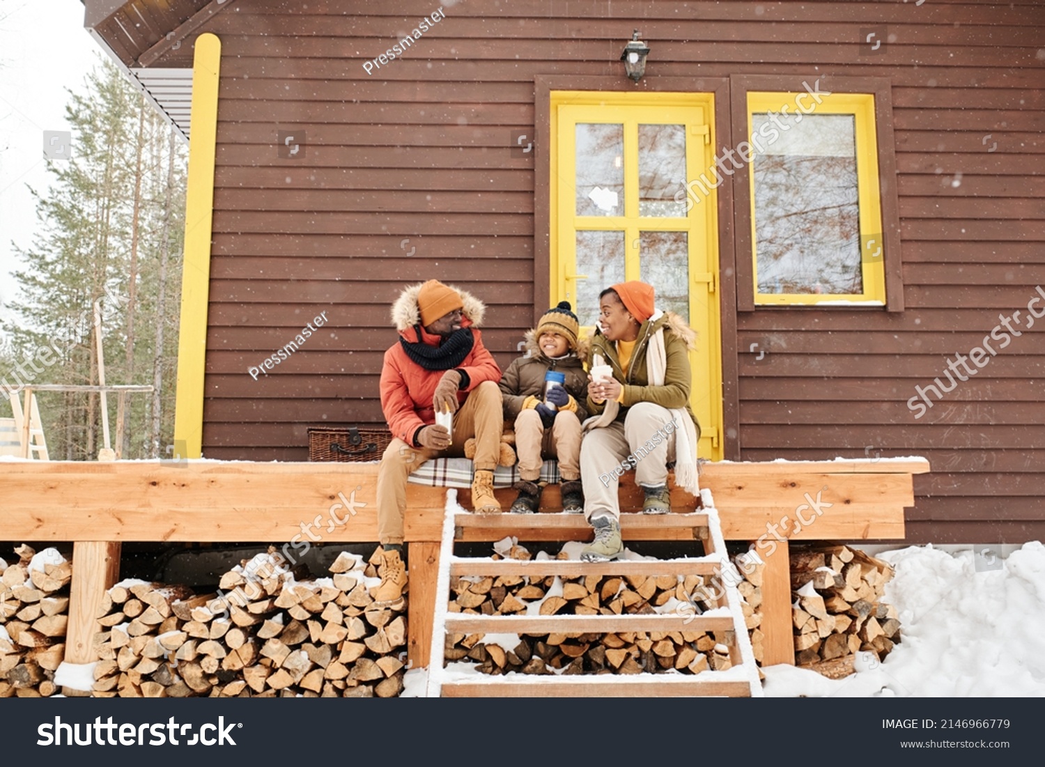 Happy young family of three sitting on wooden porch by their countryhouse, having hot tea and talking on winter day #2146966779