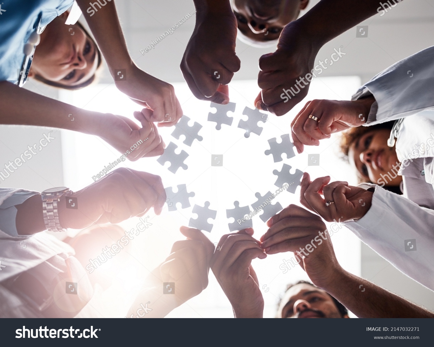Everyone plays their part here. Low angle shot of a group of doctors forming a huddle while each holds a puzzle piece inside of a hospital. #2147032271