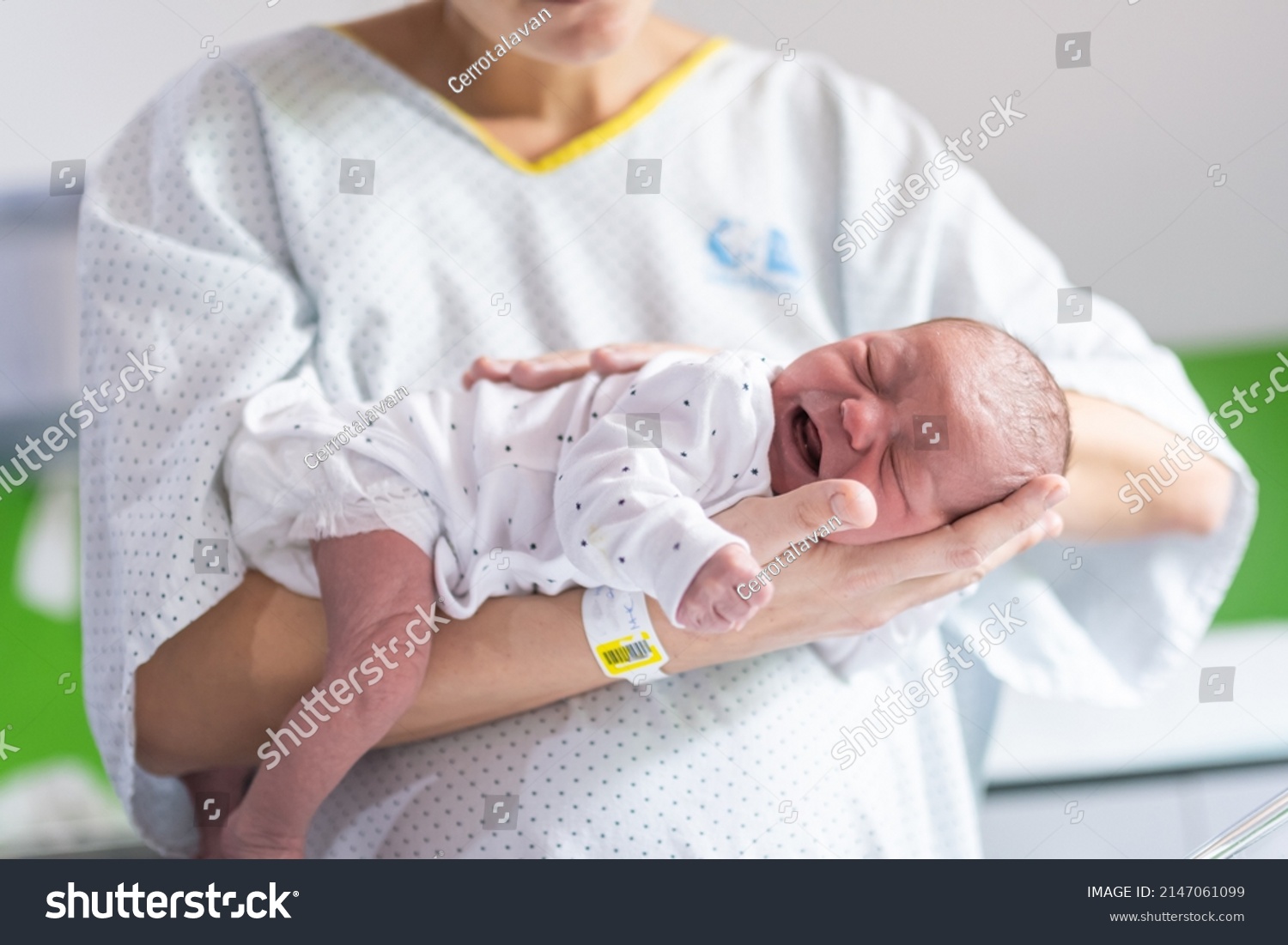 woman who has just given birth in the hospital holds her newborn baby in her arms face down to calm the crying colic of the infant. newborn care #2147061099