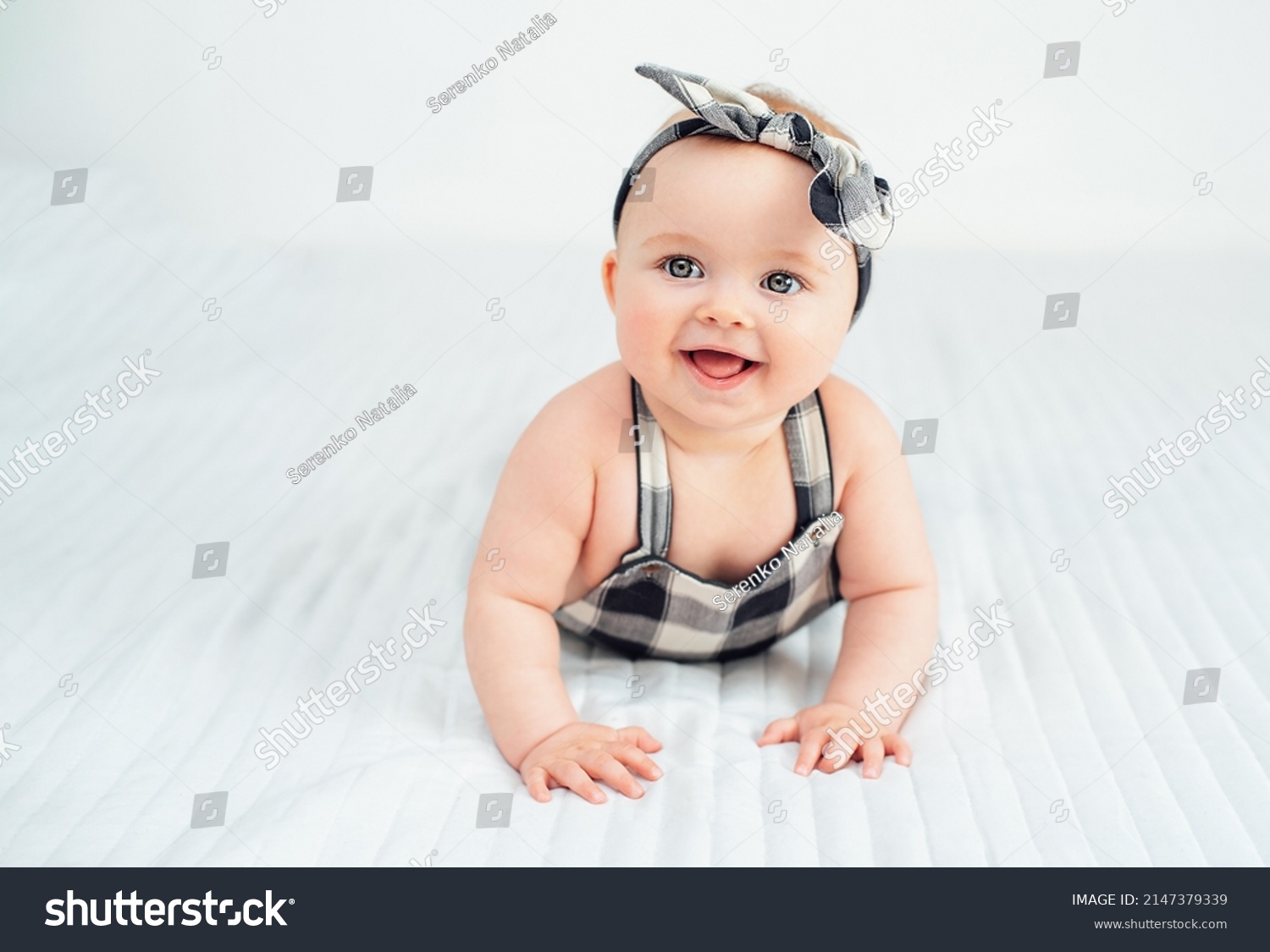 Seven month old baby child sitting on bed. Cute smiling little infant girl on white soft blanket. girl wearing headband. Charming blue eyed baby. Copy space. #2147379339