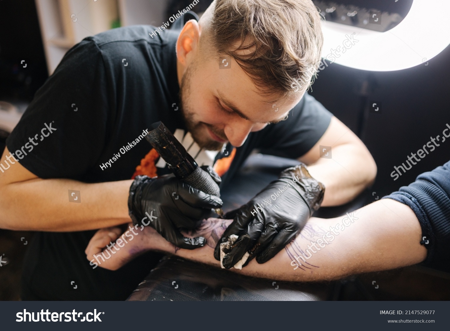 Tattoo master is tattooing a man's hand. Wireless tattoo machine, safety and hygiene at work. Close-up of tattoo artist work. Tattoo salon #2147529077