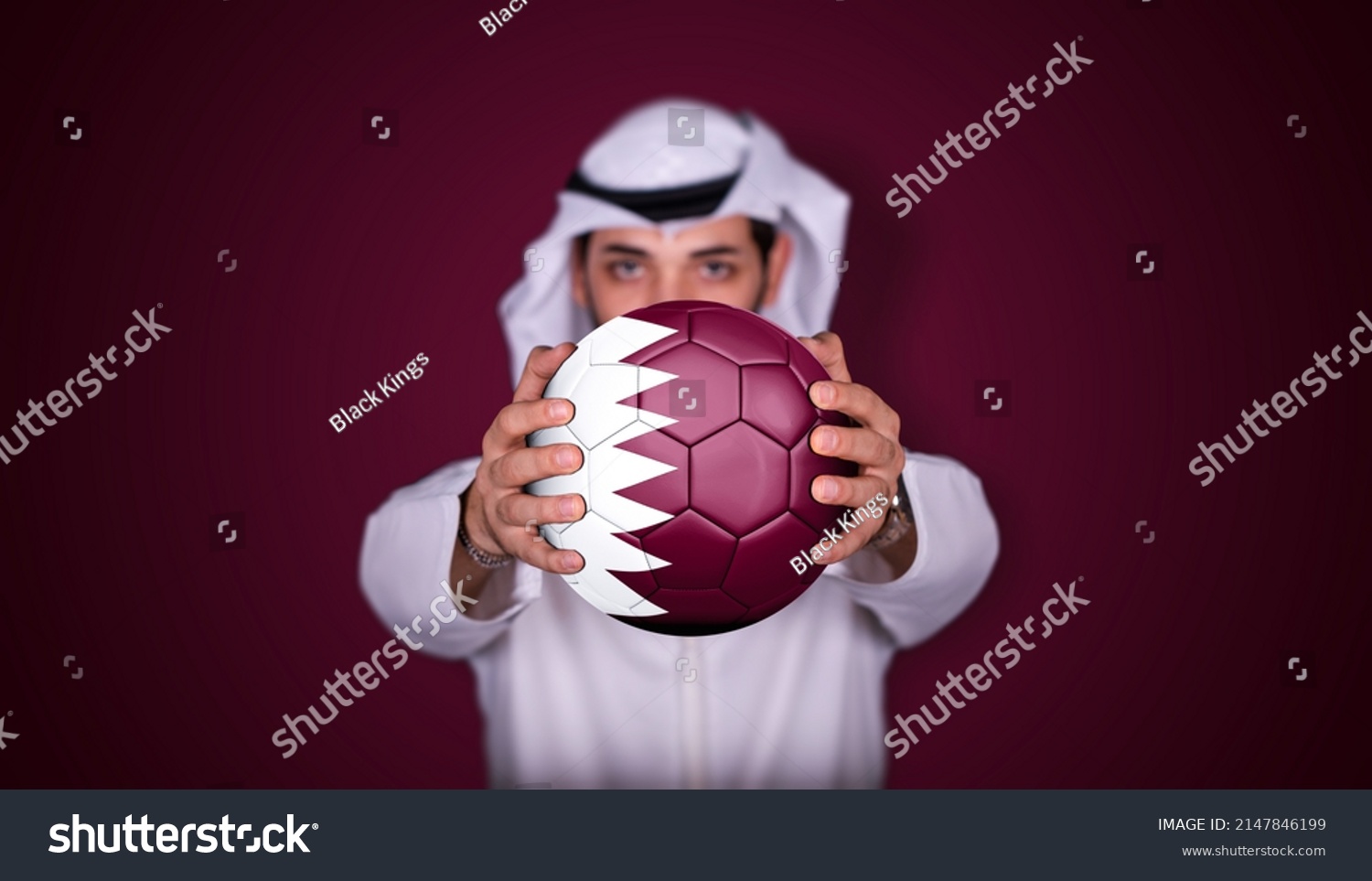 Arab man holding soccer ball in hand with Qatar flag standing on red background. #2147846199