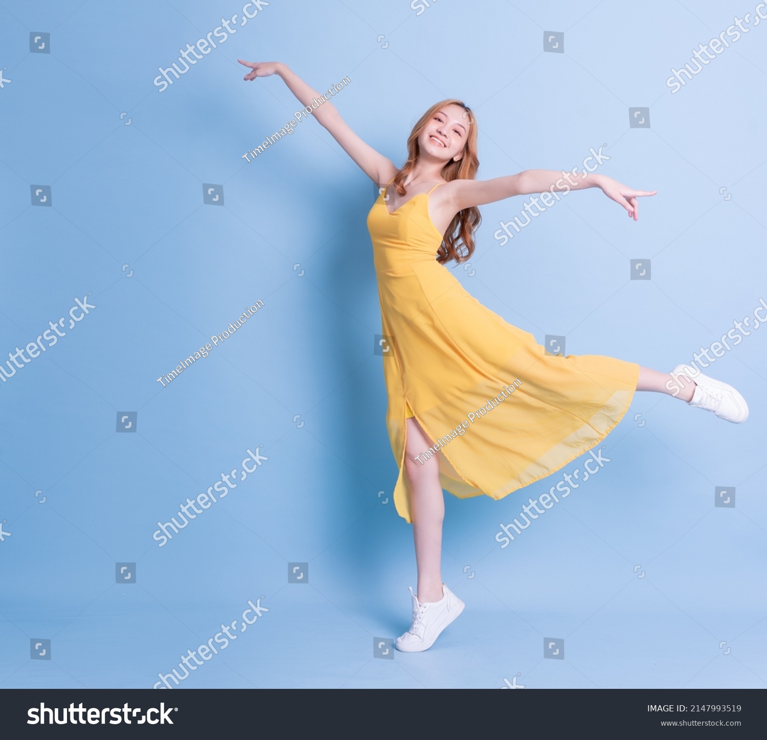 Full length image of young Asian woman wearing yellow dress on blue background #2147993519